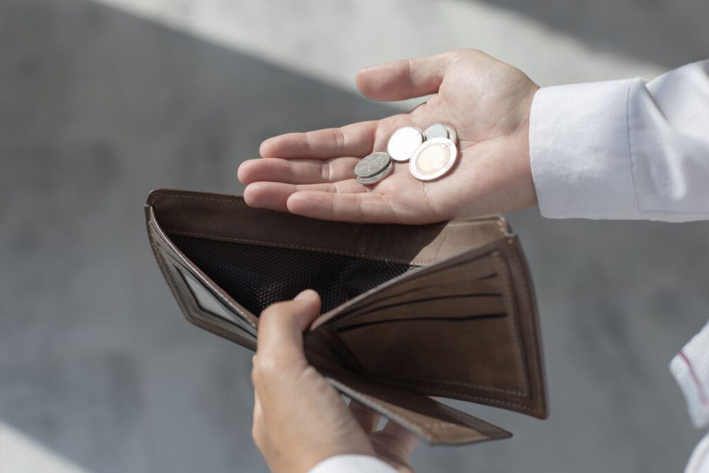 Osoba trzymająca pusty portfel i kilka monet w dłoni, symbolizująca brak pieniędzy lub problemy finansowe.