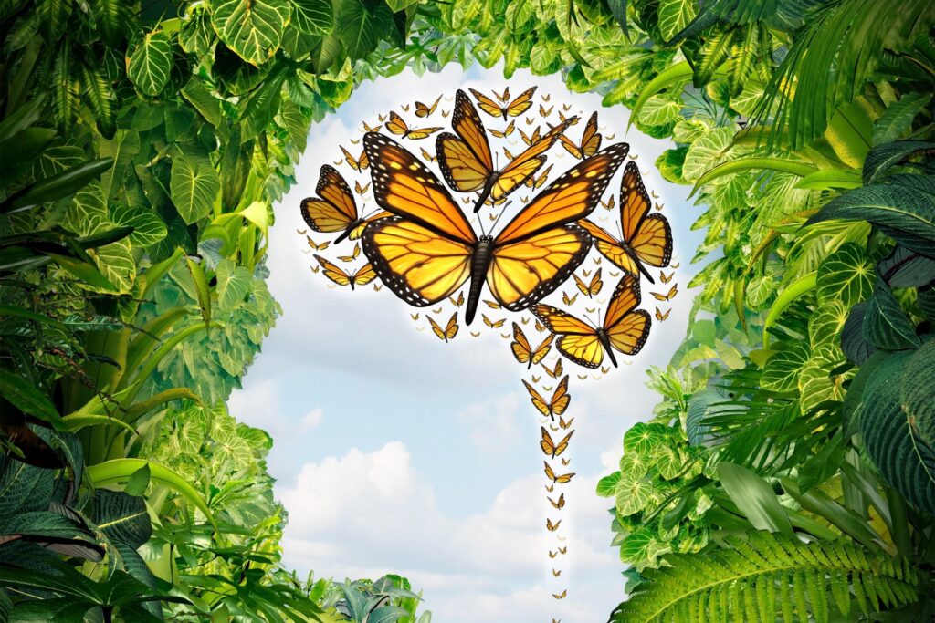 Żółte motyle wylatujące z kształtu głowy, otoczone bujną zielenią. Symboliczna grafika spokoju, wolności umysłu i wewnętrznej przemiany – wizualizacja pasująca do tematu „cytaty uważność” i rozwoju świadomości.