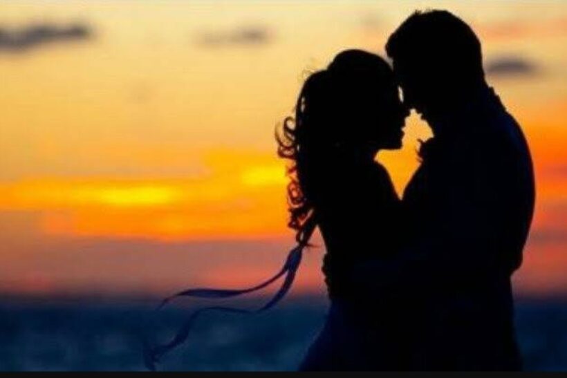 Zakochana para obejmująca się o zachodzie słońca, sylwetki na tle pomarańczowego nieba nad morzem.