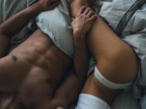 Intymna scena pary w łóżku – nagi tors mężczyzny i kobieta w białej bieliźnie pod przykryciem