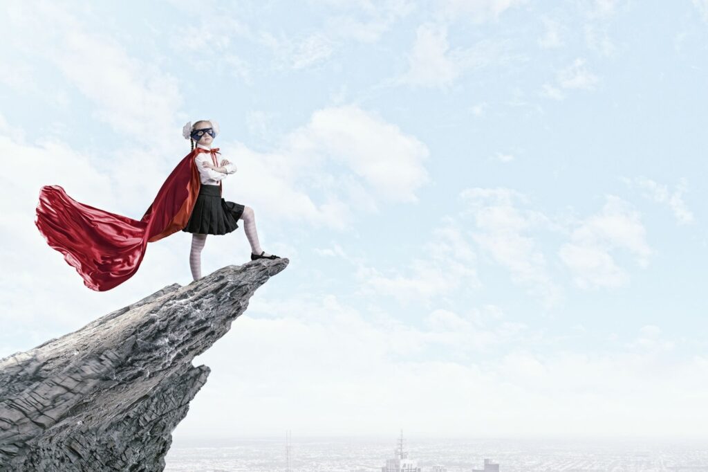 Dziewczynka w czerwonej pelerynie stojąca pewnie na skale – metafora dzielnej dziewczyny i wewnętrznej mocy