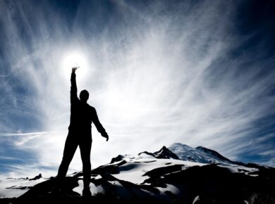 Sylwetka człowieka na szczycie góry sięgającego dłonią po słońce – symbol siły i odwagi