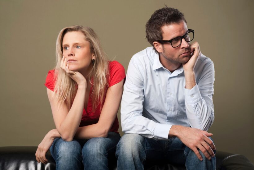 Para siedząca obok siebie na kanapie, oboje ze znudzonym i zamyślonym wyrazem twarzy.