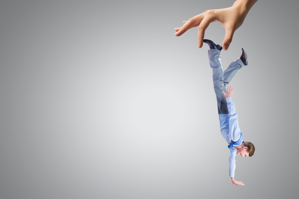 Gigantyczna dłoń trzyma mężczyznę w garniturze do góry nogami, symbolizując bezsilność i strach przed utratą kontroli.