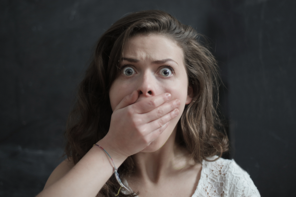 Zszokowana kobieta z szeroko otwartymi oczami zasłania usta dłonią, wyrażając strach lub zaskoczenie.
