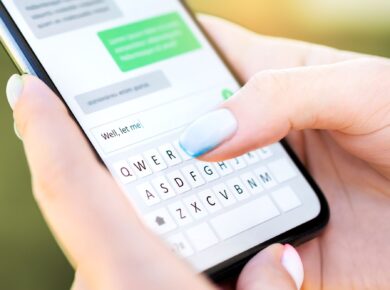 Smartfon trzymany w dłoni na tle dymków konwersacji, symbol komunikacji online i wymiany wiadomości